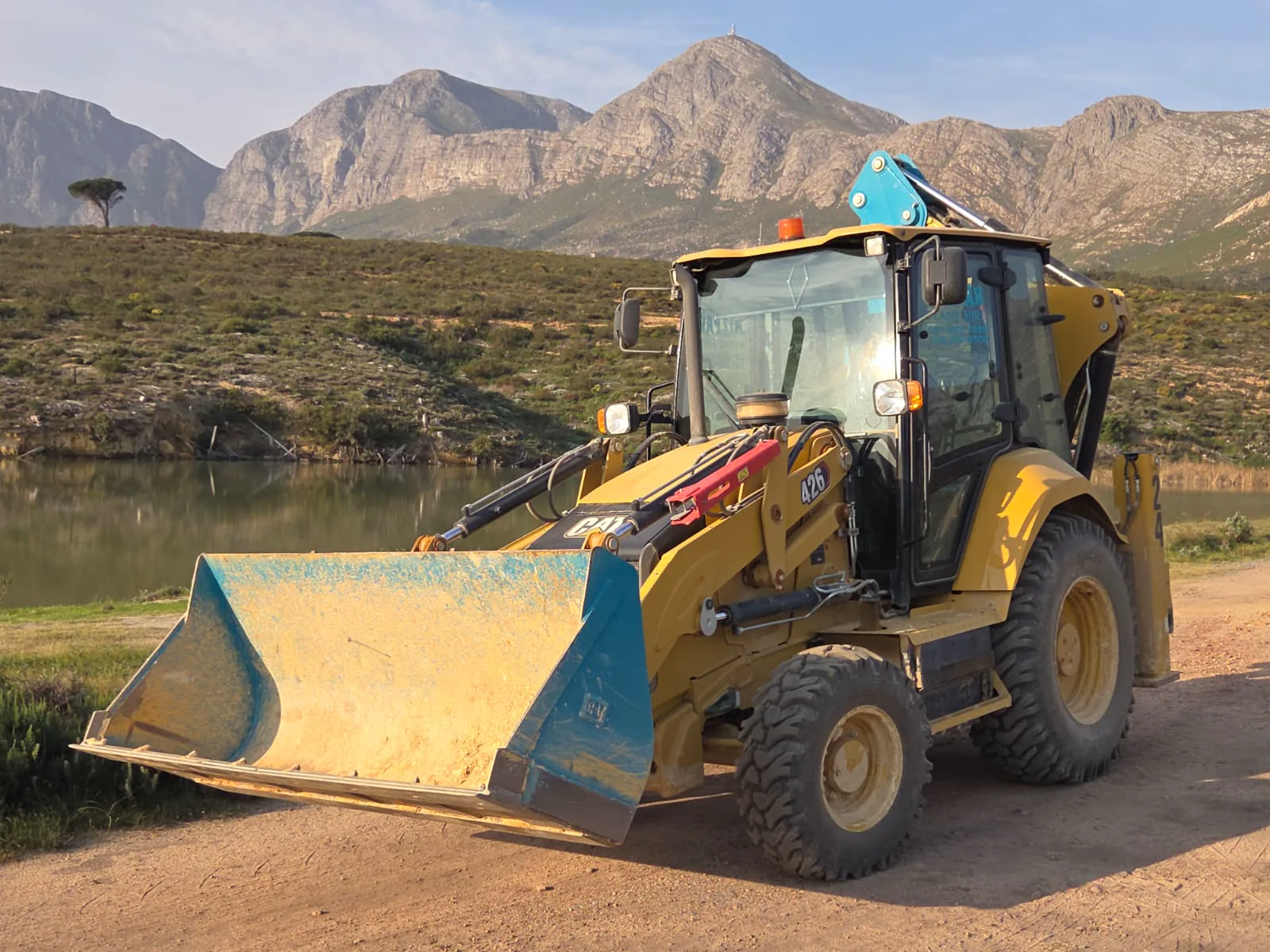 Mizpah Plant Hire TLB with its front bucket raised against the Helderberg mountains